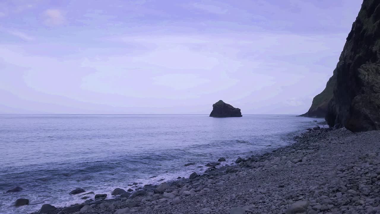 거대한 산으로 둘러싸인 해변에서 조약돌과 파도가 있는 아무도 바다 풍경 장면 움직임