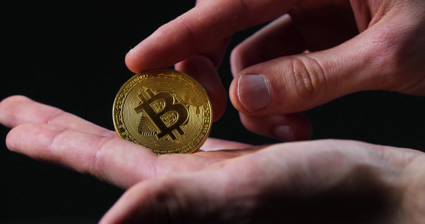 Un primo piano di mani che tengono un Bitcoin d'oro in condizioni di scarsa illuminazione su uno sfondo scuro