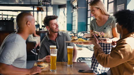 group of male friends meeting up in bar being served food by waitress