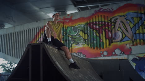 Happy-skater-relaxing-on-ramp-at-skatepark.-Handsome-man-having-break.