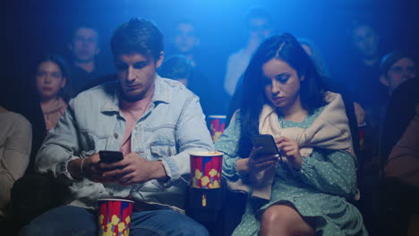 frustrated woman and man looking mobile phone screen in movie theater