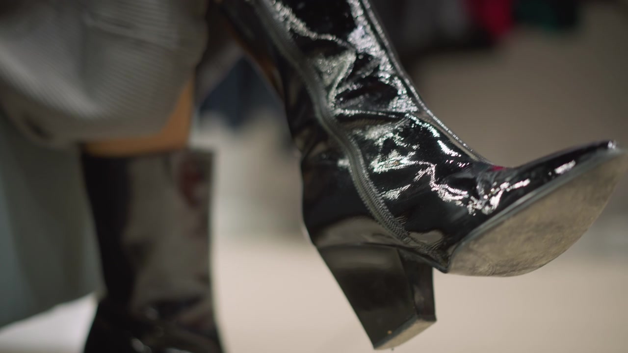 Close up of woman foot wearing shiny black patent leather boots with high heels highlighting reflective surface and stitching details. boot is shown in various positions to emphasize its