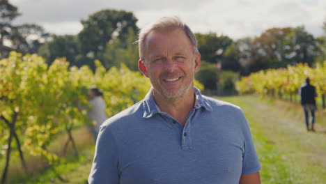 portrait of mature male owner of vineyard in field with workers at harvest