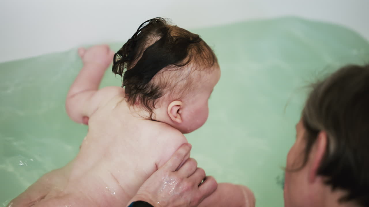 Baby enjoying bath time while being supported by a caregiver