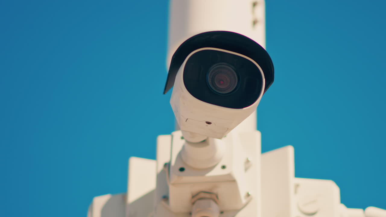 Primo piano di una telecamera di sorveglianza bianca su uno sfondo di cielo blu