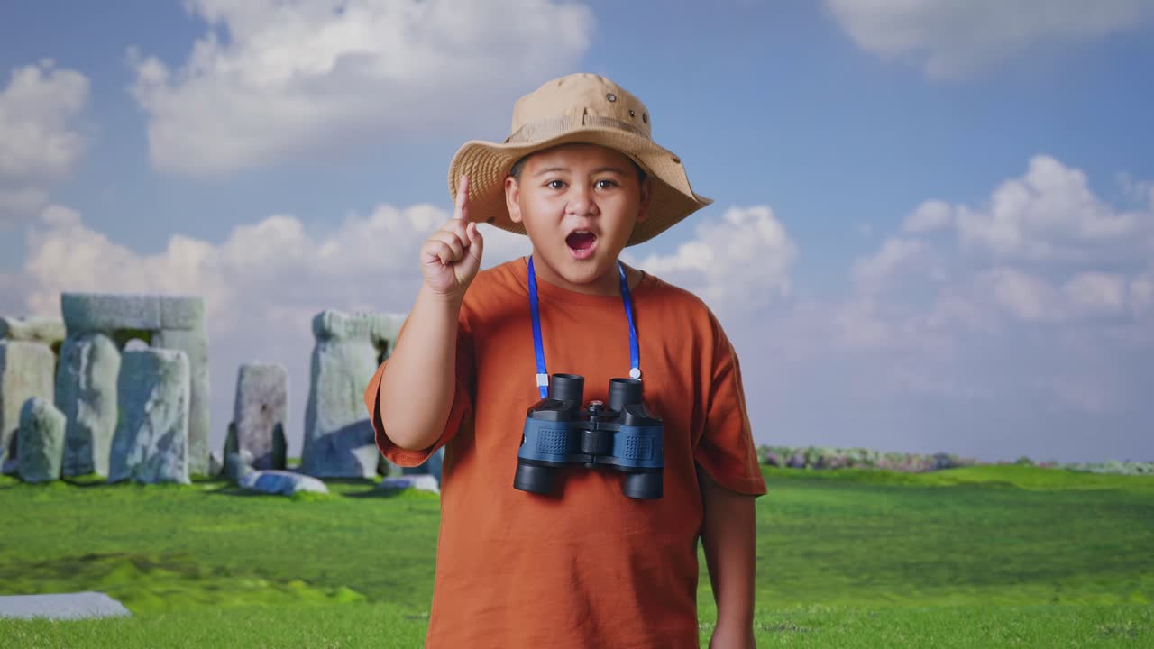 Asian Boy With A Hat And Binoculars Thinking And Looking Around Then Raising His Index Finger While Traveling In Stonehenge. Boy Researcher, Travel Tourism Adventure Concept