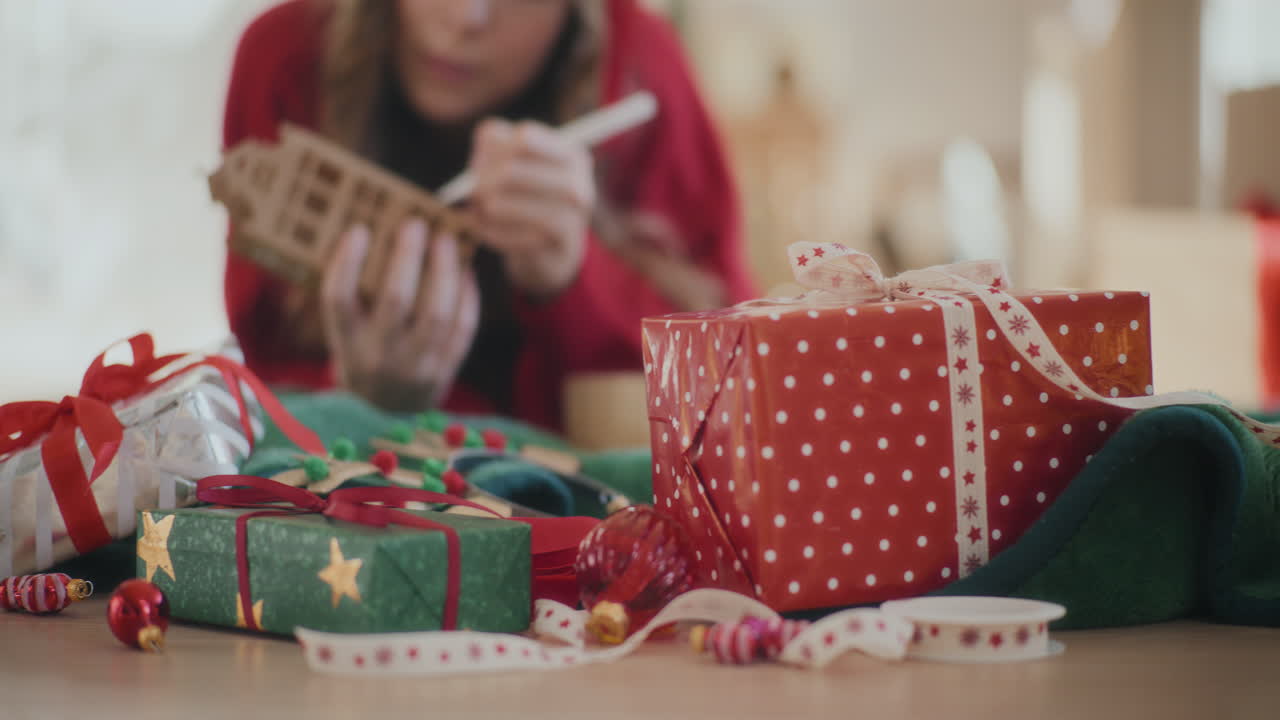 regalos de navidad envueltos en el suelo con la mujer coloreando la casa de cartón en casa