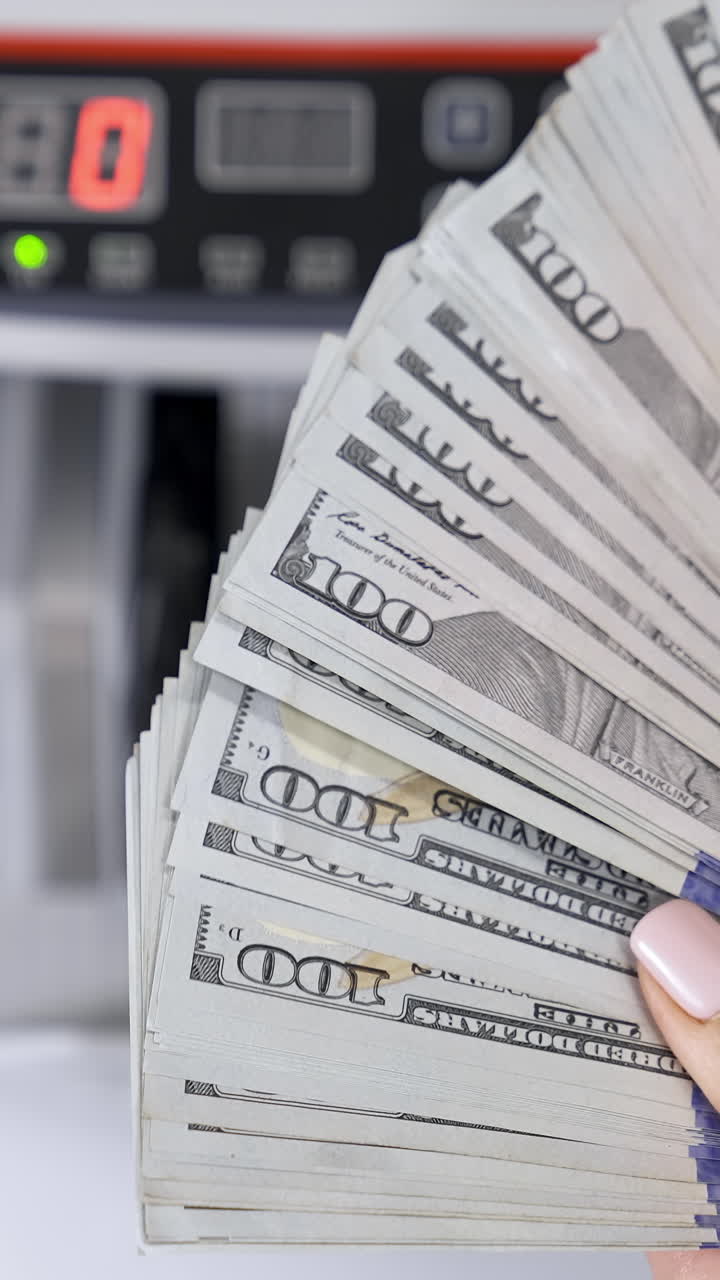 Hundred dollar bills in female's hands. Much american paper money in hands on the background of electronic calculating machine. Close-up. Vertical video