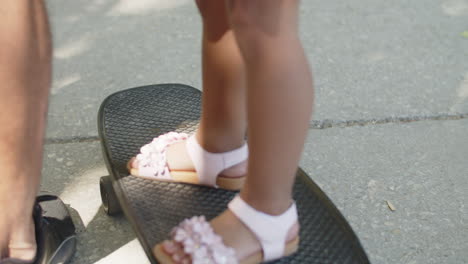 close-up of legs of little girl standing on skateboard outdoors