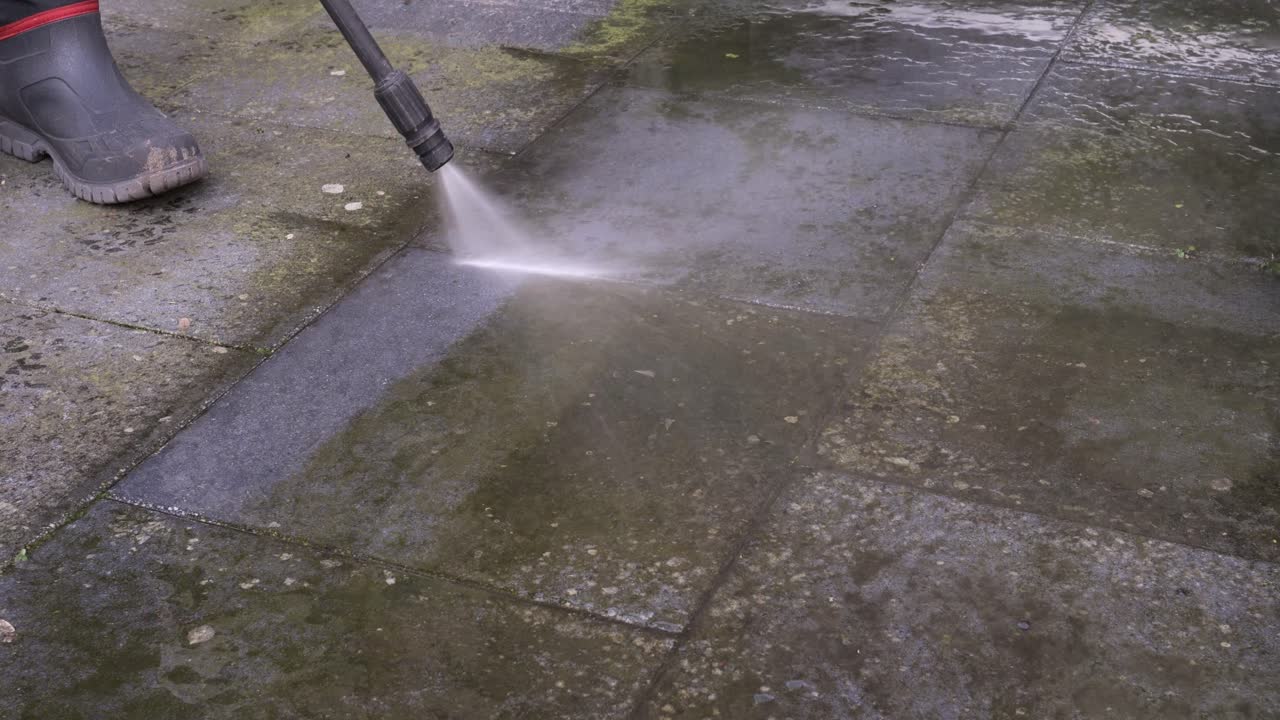 Høytrykksvasker fjerner grønnalger og smuss fra mørke terrassefliser på en uteplass. Nærbilde.