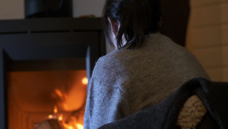 close view from behind of woman sitting by wood burning stove indoors