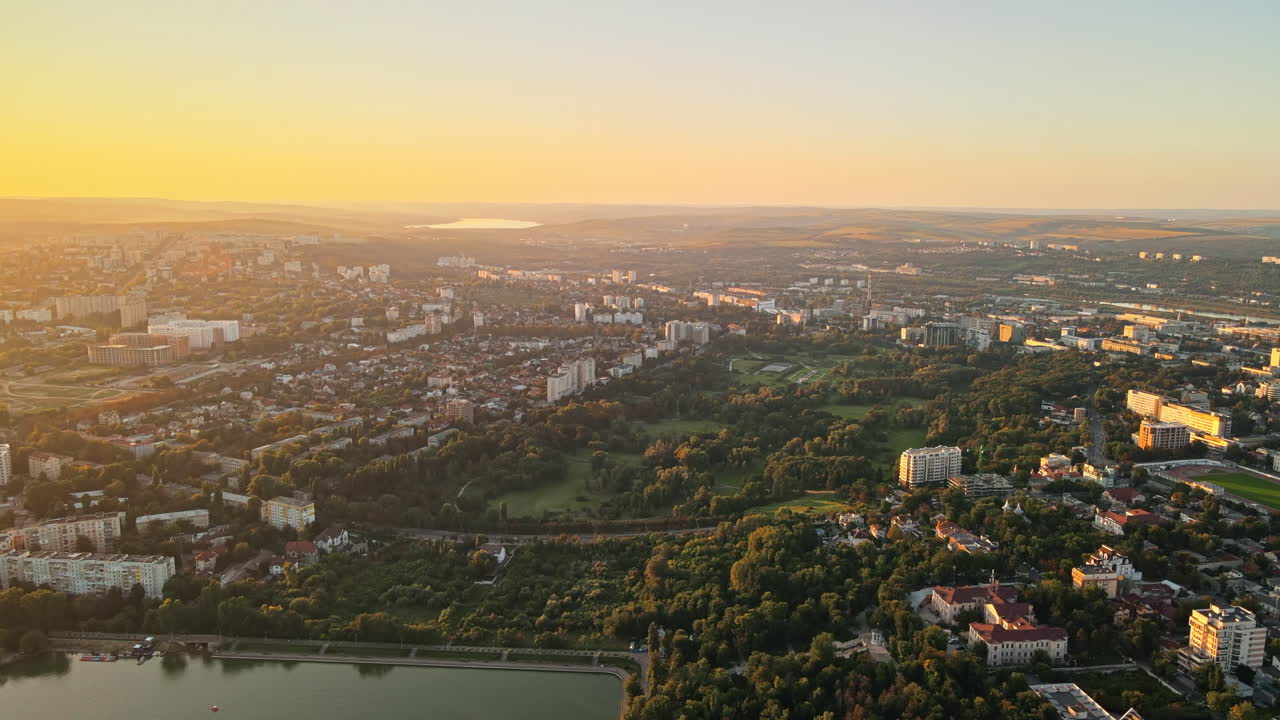 Aerial drone view of Chisinau at sunset. Panorama view of multiple buildings, lush trees and lakes, hills in the distance. Moldova