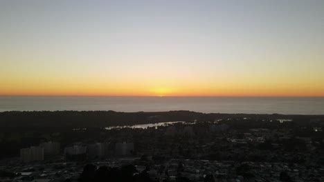 Bucle-De-Puesta-De-Sol-Sobre-El-Océano-Y-Casas-Residenciales-En-Primer-Plano-Drone-A-Través-Del-Horizonte