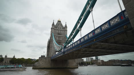 boats ride the river thames underneath tower bridge in london on a cloudy day