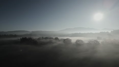 Luftaufnahme-Von-Sonnenaufgang-über-Mediterranen-Landwirtschaftlichen-Feldern-Im-Tal-Von-Barcelona,-Spanien,-Dorf-Malla-Auf-Dem-Land,-Sonnenaufgang,-Neblige-Skyline-In-Kontrastierenden-Hügeln-Und-Spärlichen-Bäumen