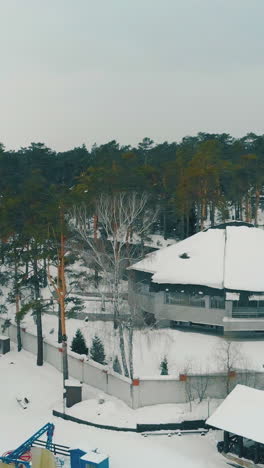comfortable hotel among old pine wood at winter resort with ski trails and surface lift under cloudy sky aerial view
