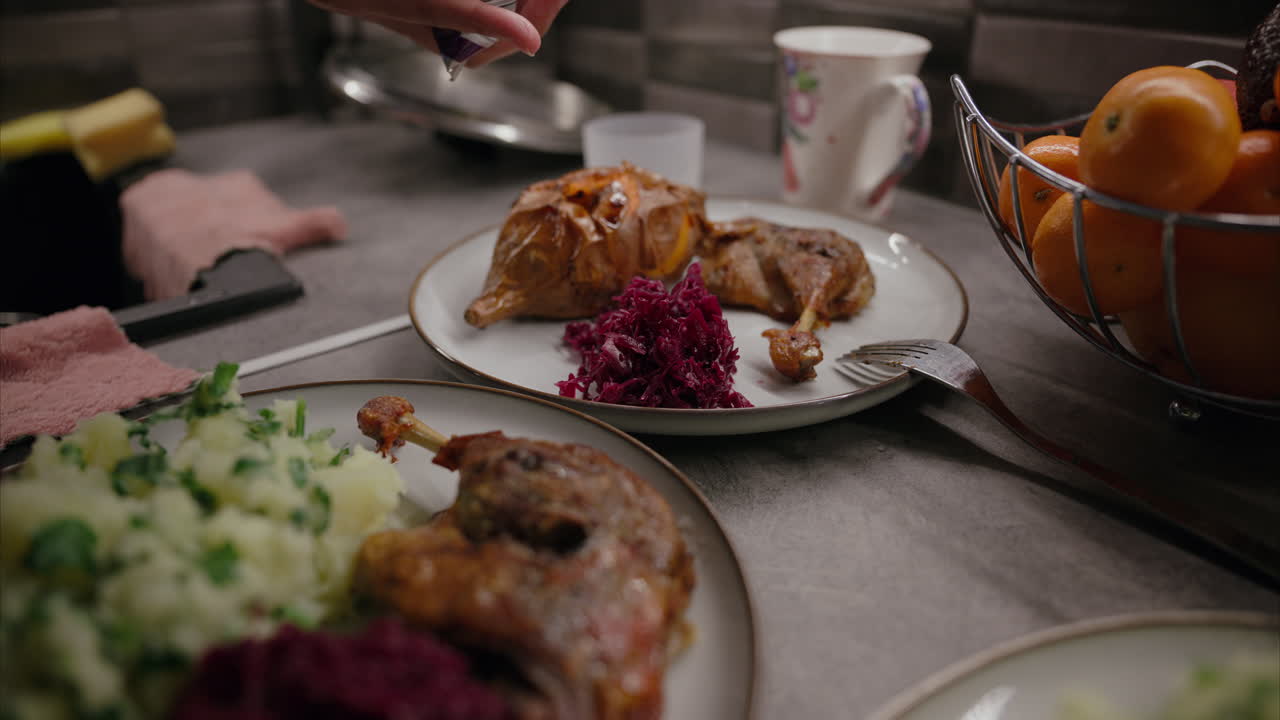 Kvinne legger rødkål på tallerkenen med spisepinner, tilbereder middag hjemme, festmat, stekt andelår, tradisjonell julemiddag, søtpotet, garnityr, tilbehør, mandarin, balansert kosthold