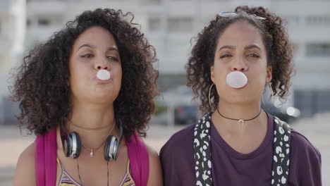 portrait attractive hispanic twin sisters blowing bubblegum enjoying summer vacation together smiling cheerful siblings in sunny urban city slow motion