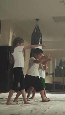 los niños hacen puñetazos con el entrenador en la escuela de lucha. los niños pequeños aprenden técnicas de autodefensa con un joven instructor en el gimnasio en cámara lenta. deporte de boxeo