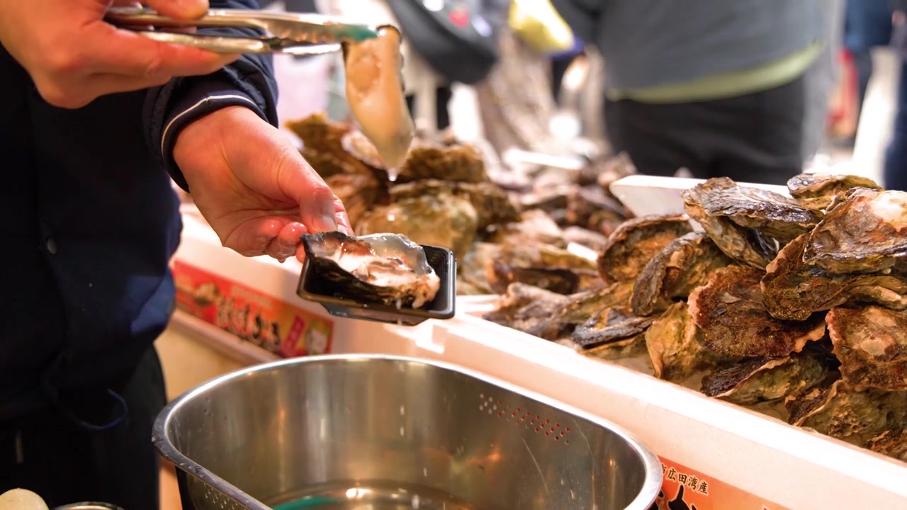 A seafood vendor uses tongs to place fresh oysters onto a tray for a customer.