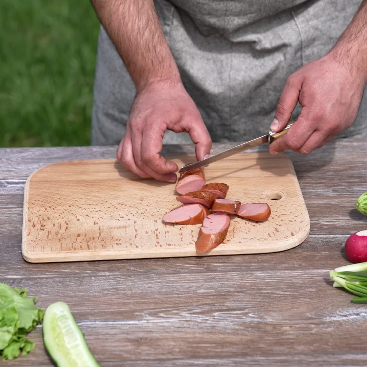 Man cutting barbeque sausage for picnic. Tasty lunch at grill outside