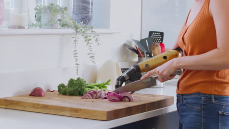 primer plano de una mujer con un brazo protésico en la cocina preparando comida y cortando cebolla