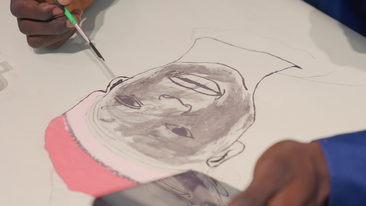Tangan melukis potret berwarna gelap di atas kertas dengan kuas dan arang, foto studio jarak dekat menunjukkan bayangan dan tekstur detail, seniman mengacu pada foto ponsel saat menambahkan warna topi merah muda, terfokus.