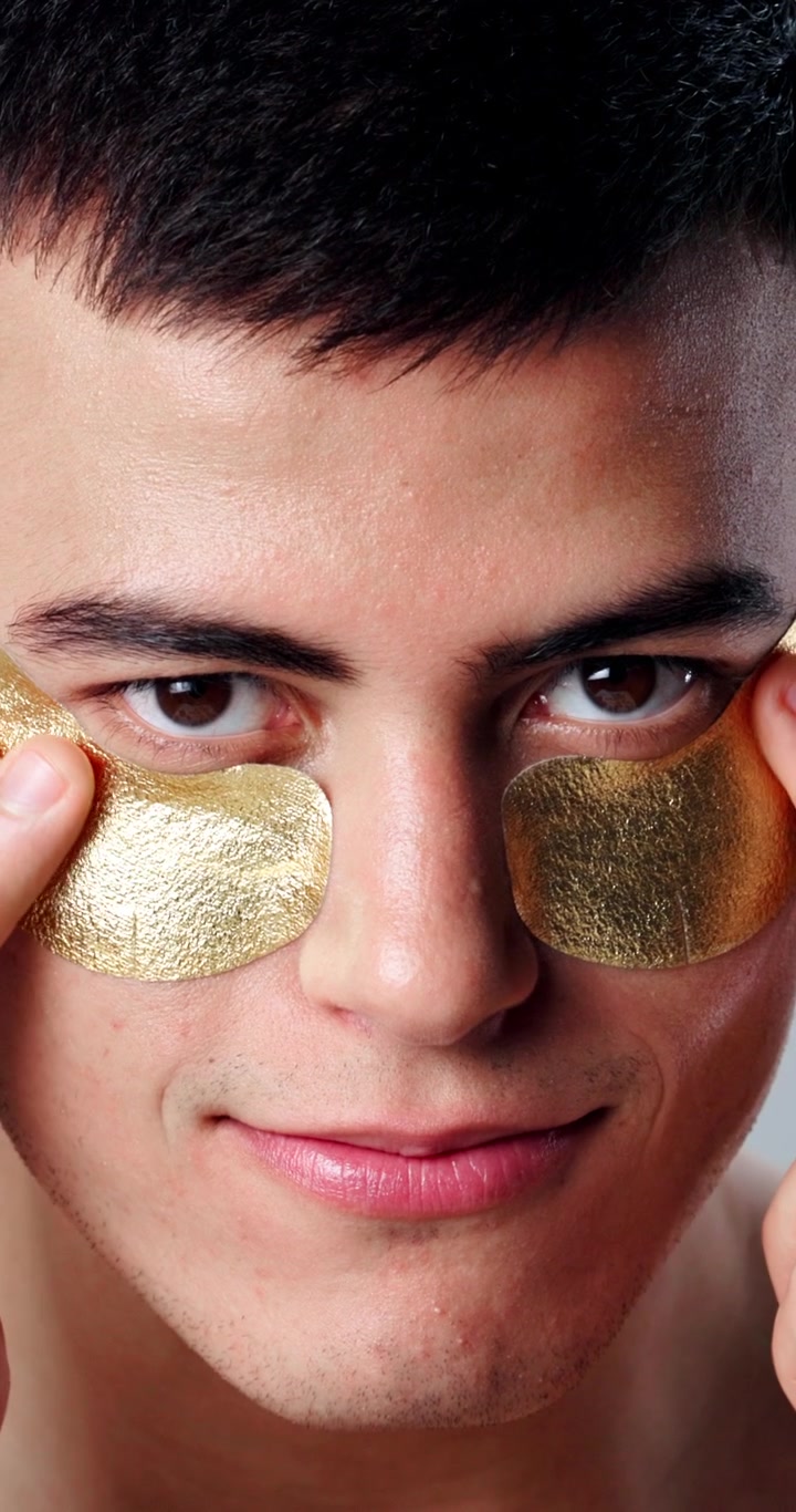 Young Man Applying Gold Under-Eye Patches for Skincare