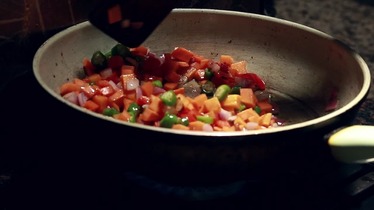 Stir-frying vegetable cubes ingredient for fried rice recipe in a pan using a wooden spatula, candid healthy home cooking