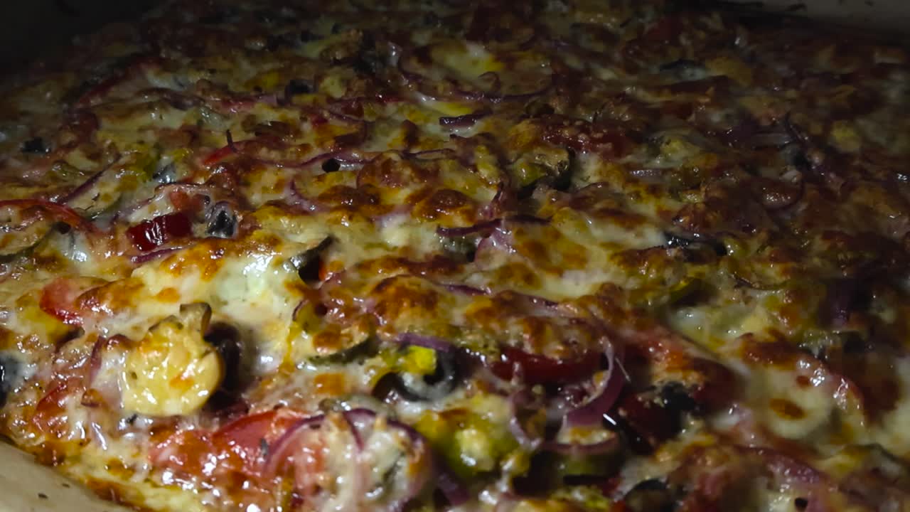 Primo piano con ripresa orbitale intorno a formaggio grigliato e al forno e condimento per pizza sotto e dentro, in una cucina casalinga con una buona illuminazione. Pomodori, jalapeño, olive nere
