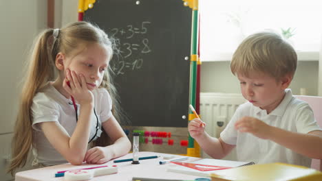 elder sister looks at brother drawing figure with ruler