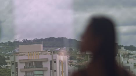 Pull-focus-on-woman-enjoying-view-outside-her-apartment-window-on-an-overcast-day,-slow-motion