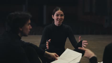 una feliz chica morena en un traje negro una actriz se sienta en el escenario y se comunica con sus colegas durante un ensayo y preparación para una actuación en el teatro