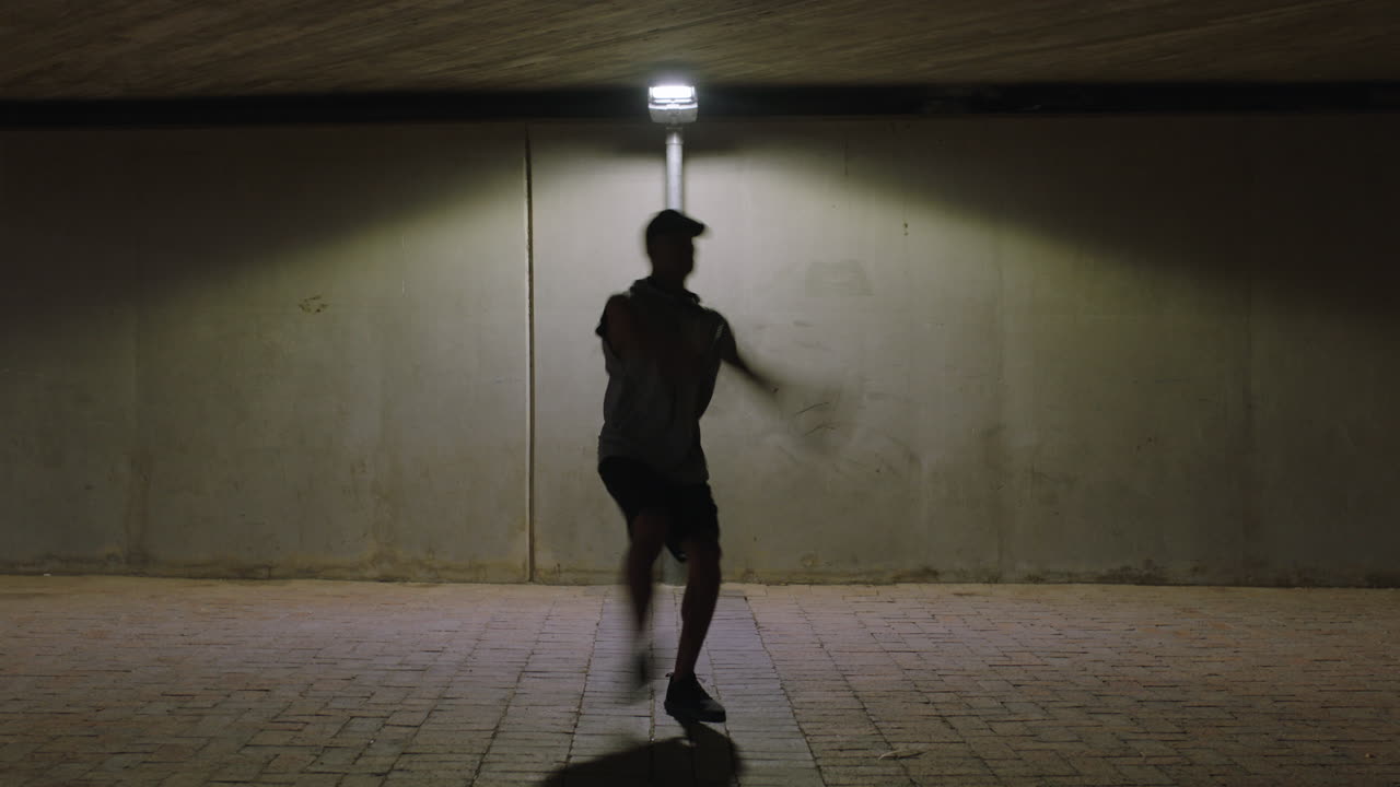 hombre bailando joven breakdancer realizando movimientos modernos de baile hip hop bajo la luz de la calle practicando coreografía de estilo libre urbano en la ciudad por la noche