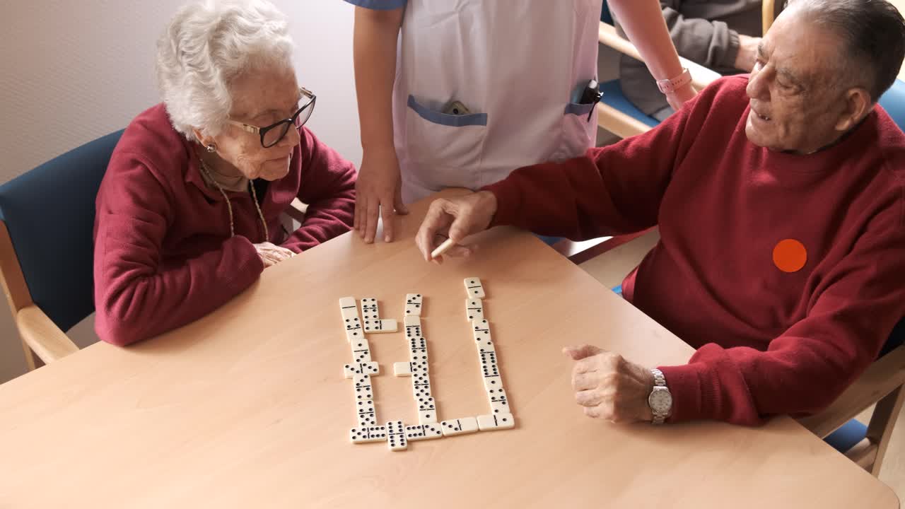 Nurse playing dominoes with senior man and woman in canteen of nursing home