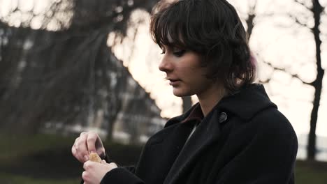 Young-woman-in-a-black-coat-sitting-in-a-park-in-autumn-in-afternoon-and-feeding-ducks-in-a-sea-2