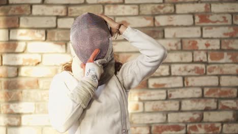 fencer in action posing in front of a brick wall