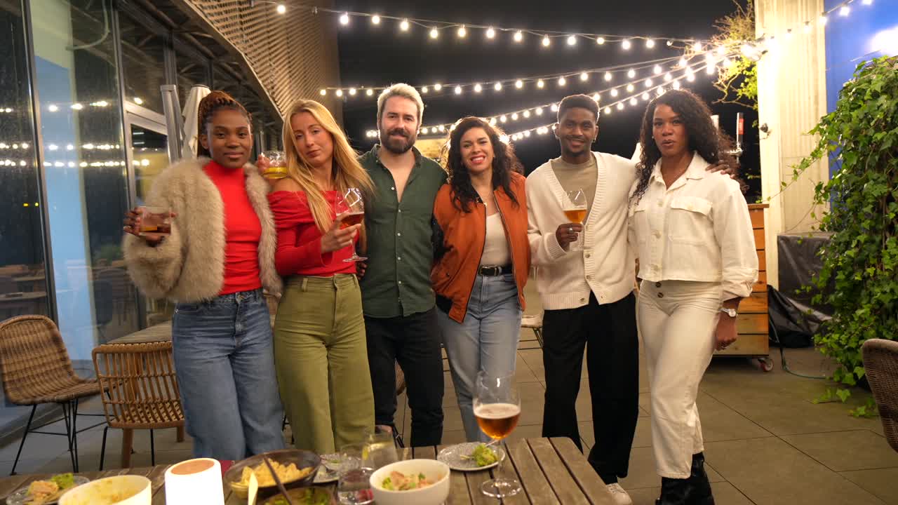 Group of friends enjoying an outdoor gathering with drinks and food under string lights