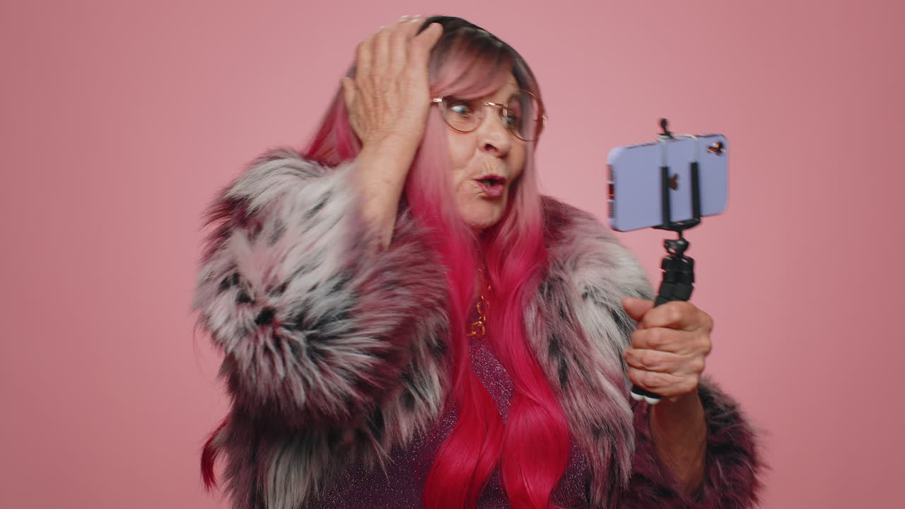 여성 블로거가 스마트폰으로 셀카를 찍고 셀카 스틱으로 구독자와 온라인으로 비디오 통화를 통신합니다.