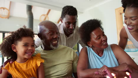 Multi-Generation-Family-Celebrate-Grandmother's-Birthday-With-Cake-And-Candles-Around-Table-At-Home