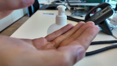 close-up of liquid sanitizer being dispensed into palm at office desk