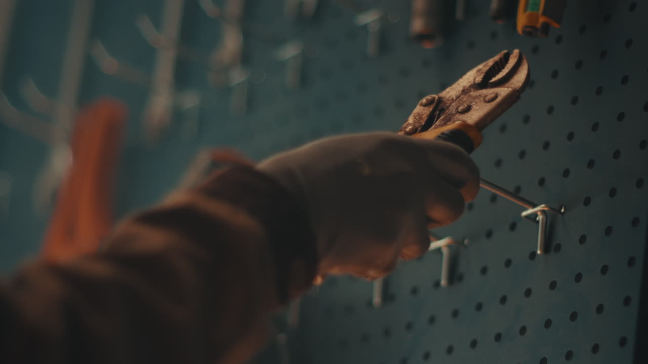 Mechanic placing pliers returning back to tool wall inside workshop close up telephoto details, slow motion