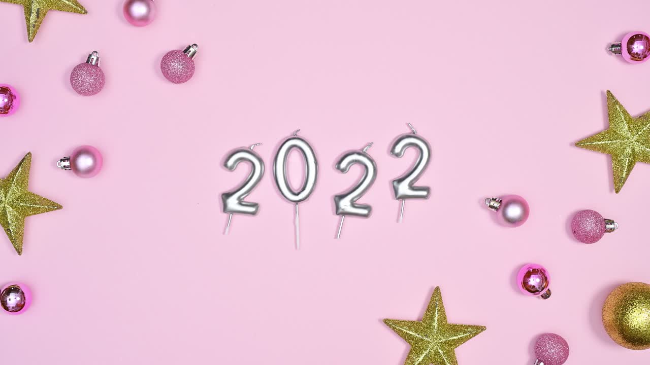 Decoración navideña hecha de adornos navideños y el número 2022 se mueven sobre un tema rosa pastel. Stop motion