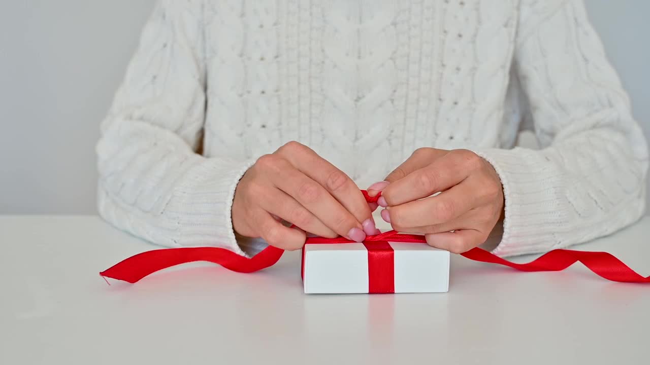 Mani femminili legano il fiocco rosso di una scatola regalo con incarto bianco
