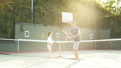 man teaching his little daughter how to play tennis on a summer day 1