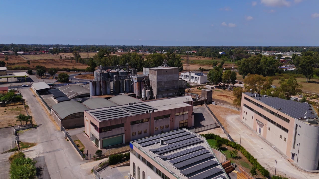 Vista aerea di un grande complesso industriale con edifici, silos e pannelli solari installati sui tetti. Energia sostenibile in una fabbrica.