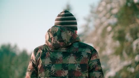 a person wearing a camouflage jacket walks on a forest pathway covered in snow on a winter day