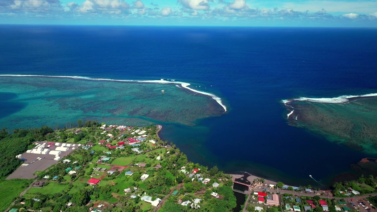 Ripresa aerea con drone di Teahupoo, Tahiti, Polinesia Francese: Papeete al mattino con sole splendente, barca, baia, canale, barriera corallina. Sede del surf per le Olimpiadi di Parigi 2024, con nuova torre dei giudici e ponte pedonale, vista dall'alto in avanti.