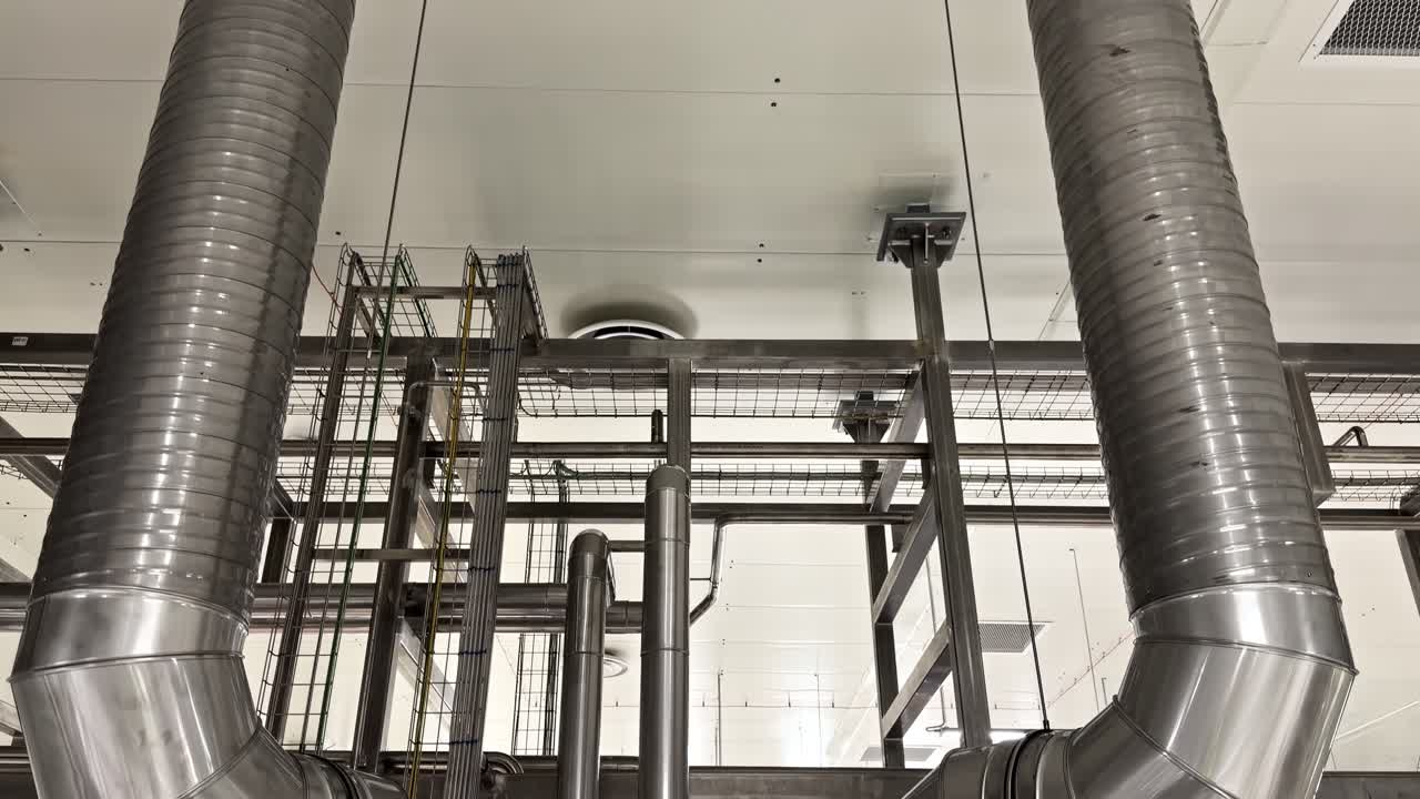 White industrial ceiling with pipes, ducts, and lighting fixtures in clean modern facility, tilt down