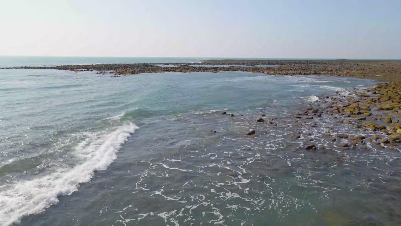 Vista aérea da costa. Ondas quebrando em corais. Ilha rochosa no meio do vasto oceano. Drone voando sobre a água do mar, tomada de dolly para frente.